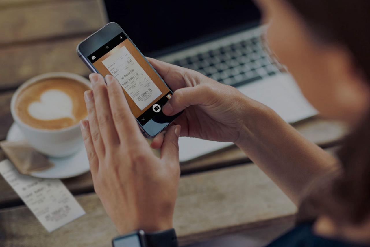Picture of business owner out for a coffee and working remotely whilst adding receipt to app on mobile for bookkeeper.